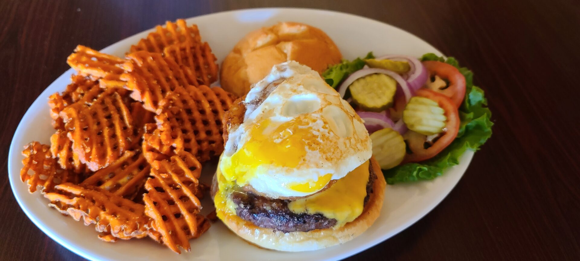 A plate of food with an egg sandwich and some potato waffles.